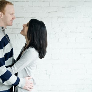 candid portrait of an engaged couple standing in front of a white brick wall