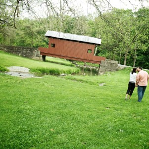 couple takes a walk in an open field towards a red covered bridge in washington, pa