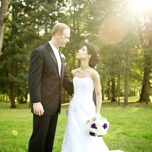 newly weds hold hands in a park as sunlight streams in behind them