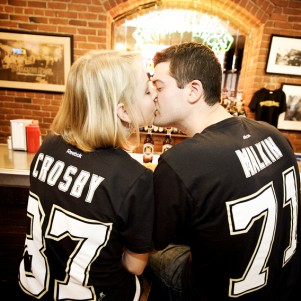 engaged couple wearing pittsburgh penguins t-shirts kissing at the bar inside of primanti's in the strip district