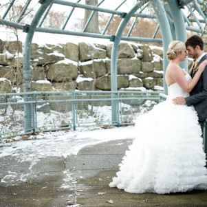 groom holding bride against railing outside during winter